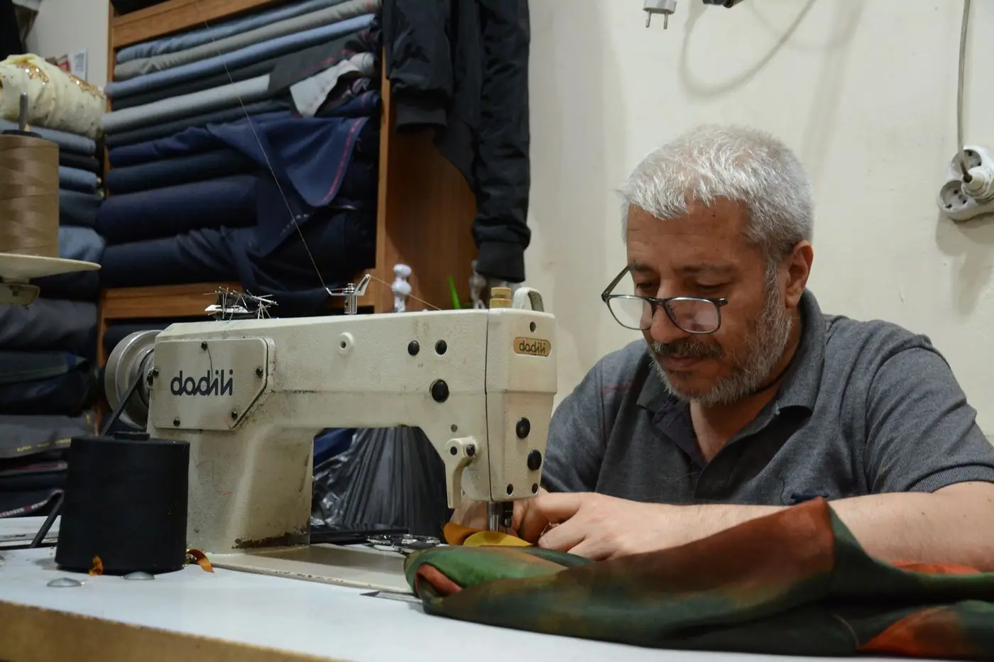 A tailor operating a sewing machine, surrounded by fabric
