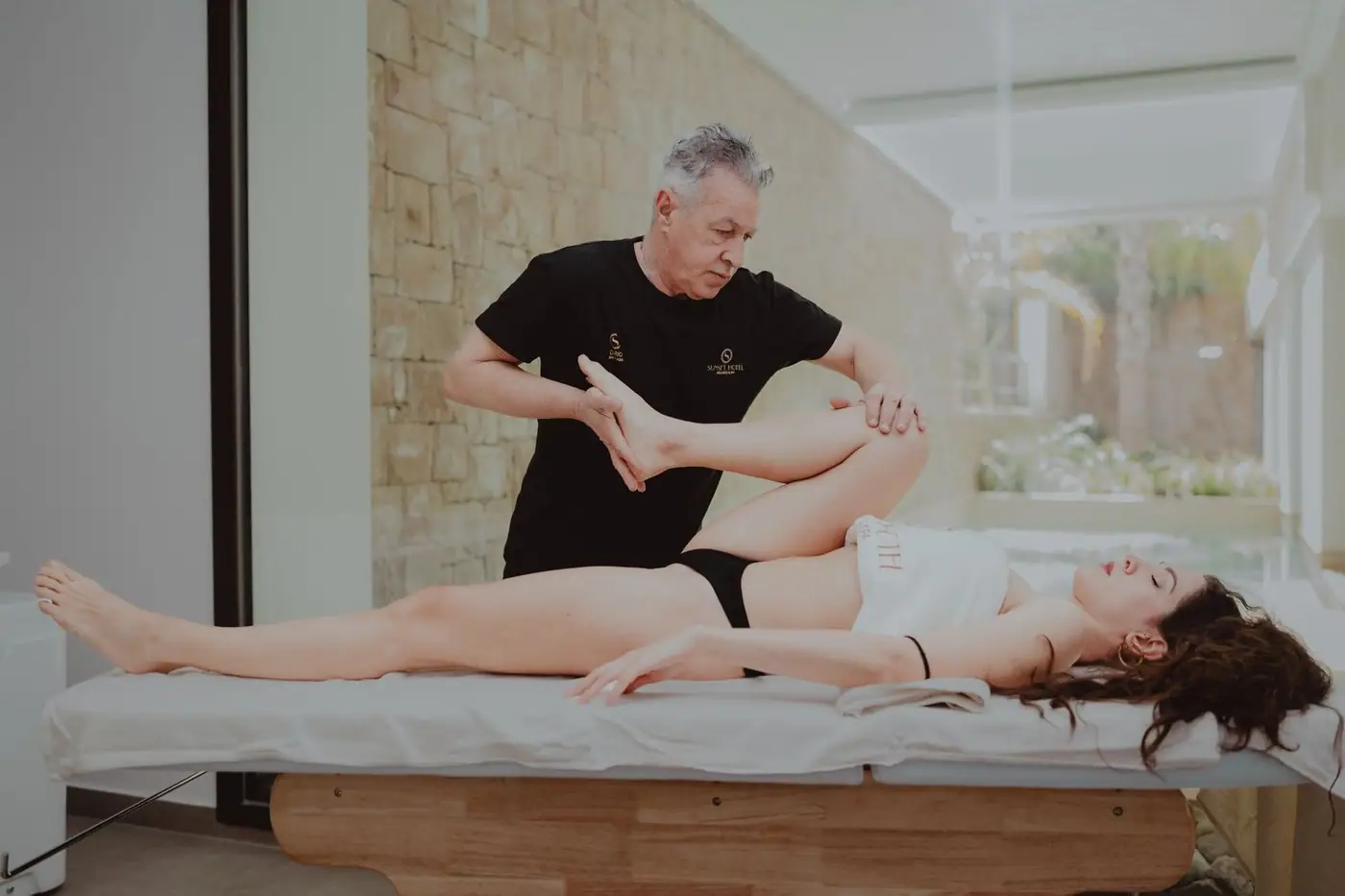 A therapist assists a patient during a rehabilitation session indoors, helping with mobility and flexibility.