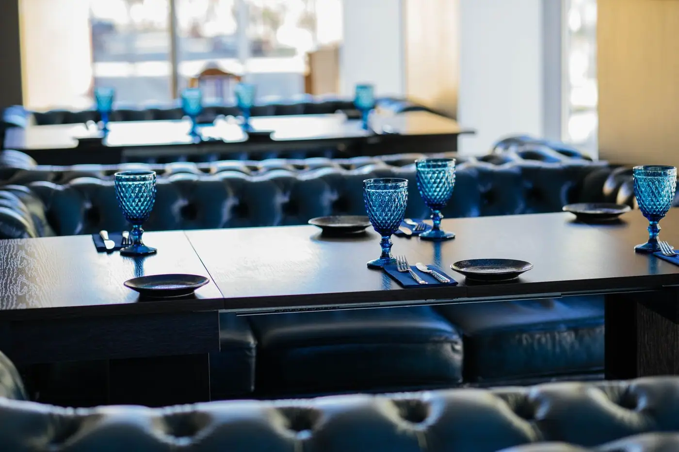 Elegant blue wineglasses served on a wooden table with plates and silverware in a cosy restaurant with leather sofas