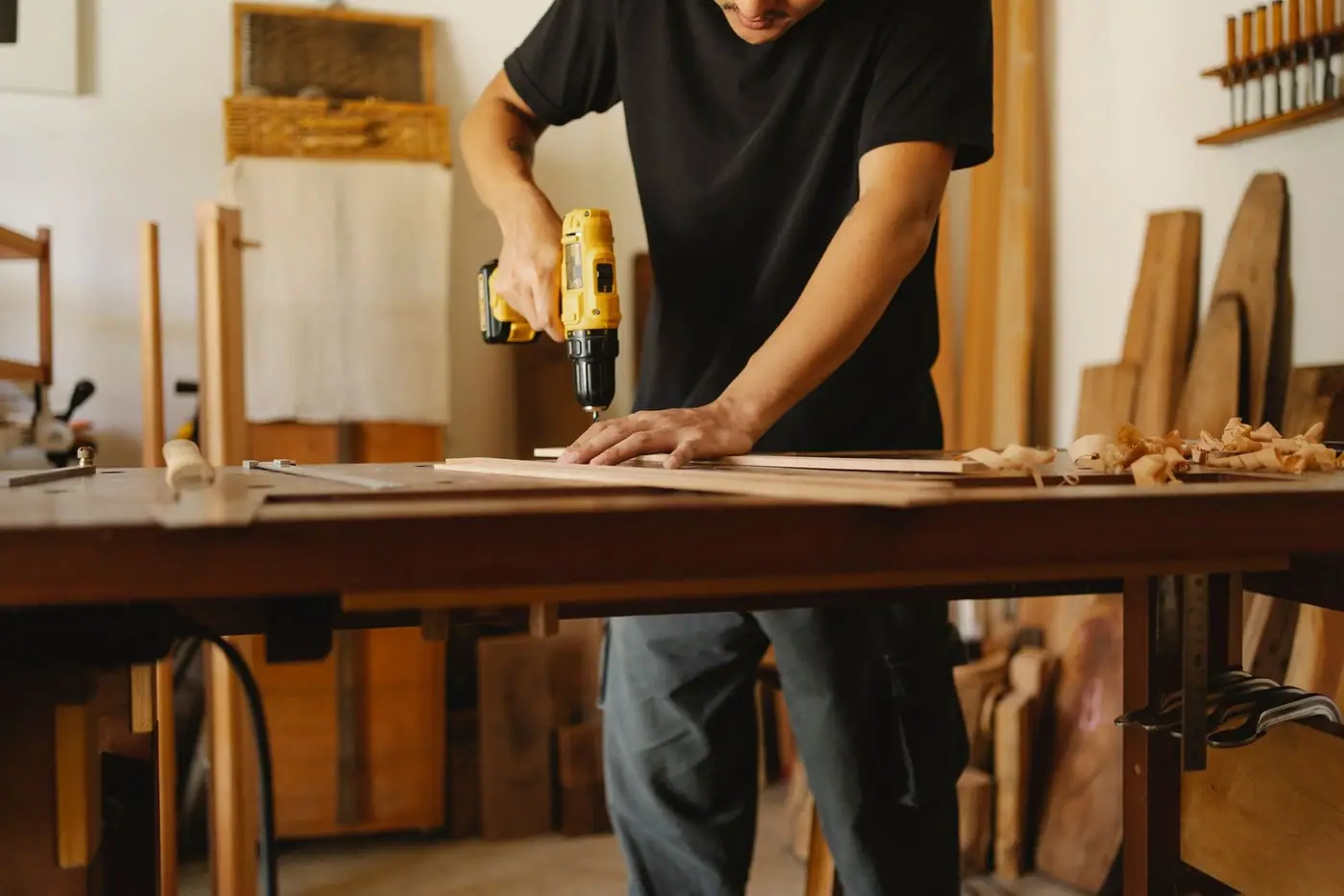 A man in casual clothes drilling at a workbench in a joinery workshop