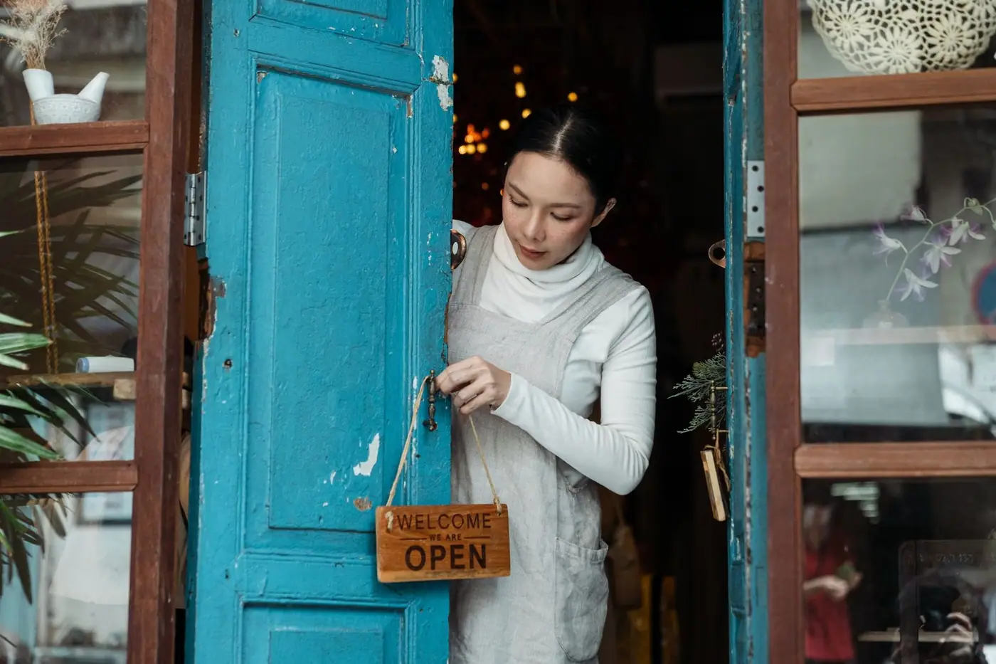 A woman adjusts an open sign on a blue wooden door
