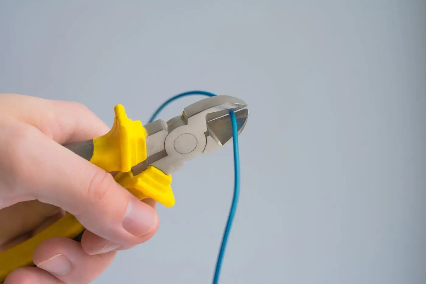 A hand using pliers to cut a blue wire against a grey background