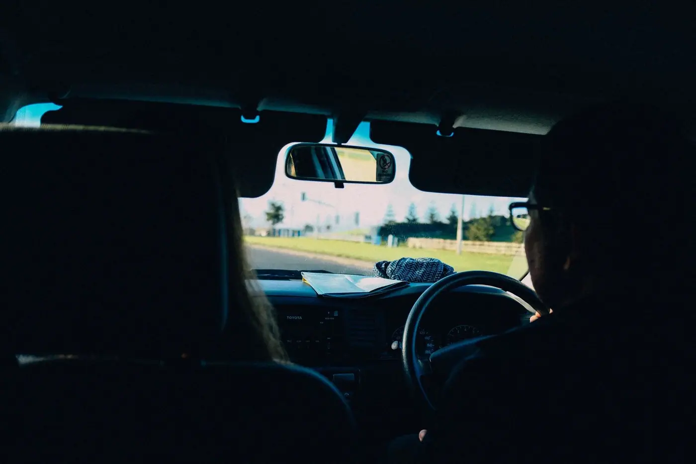 Back view of a person driving a right-hand-drive car, with a passenger in the front seat