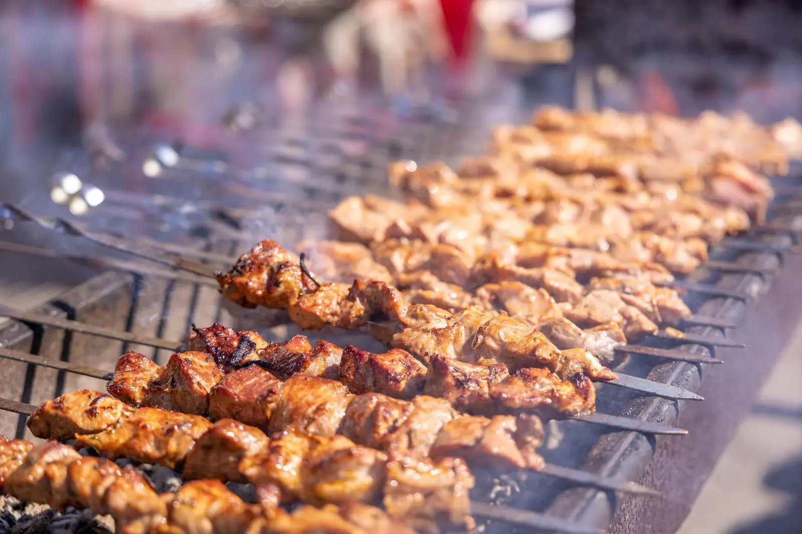 Close-up of sizzling grilled meat skewers on barbecue grill outdoors.