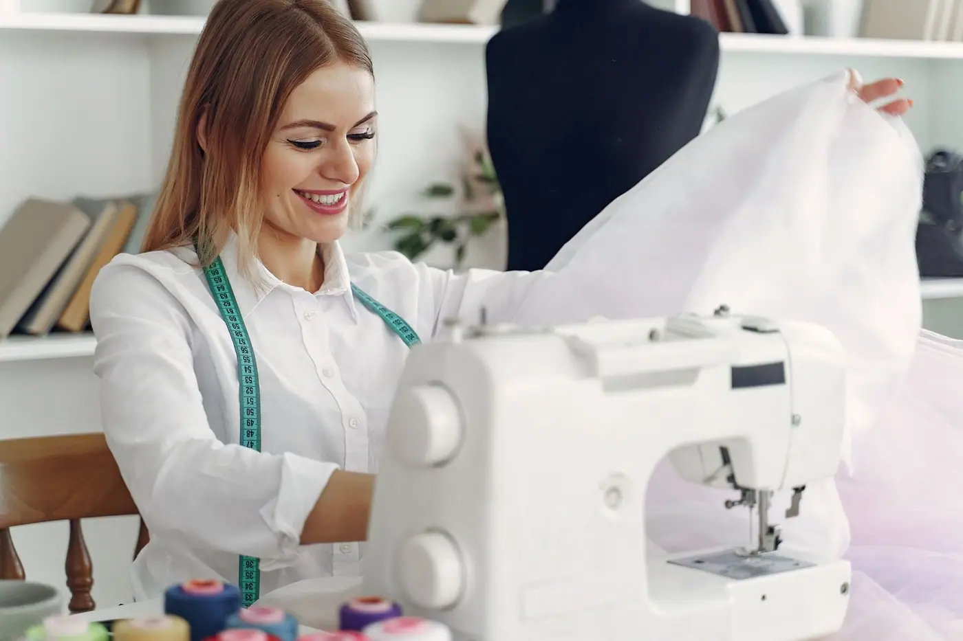 A smiling designer working on a sewing machine with fabric in a bright studio