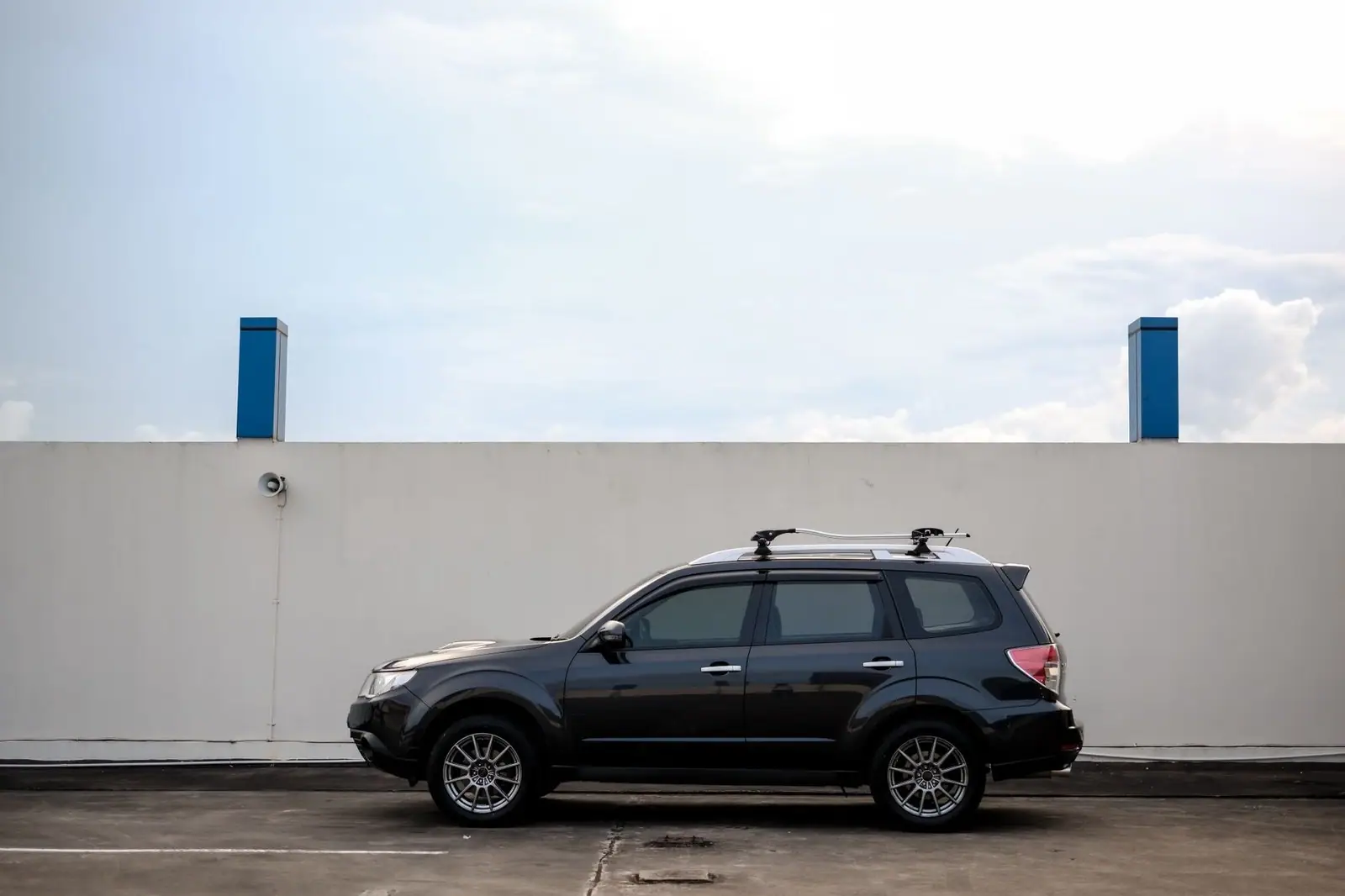 Side view of a black SUV parked in front of a white concrete wall under daylight