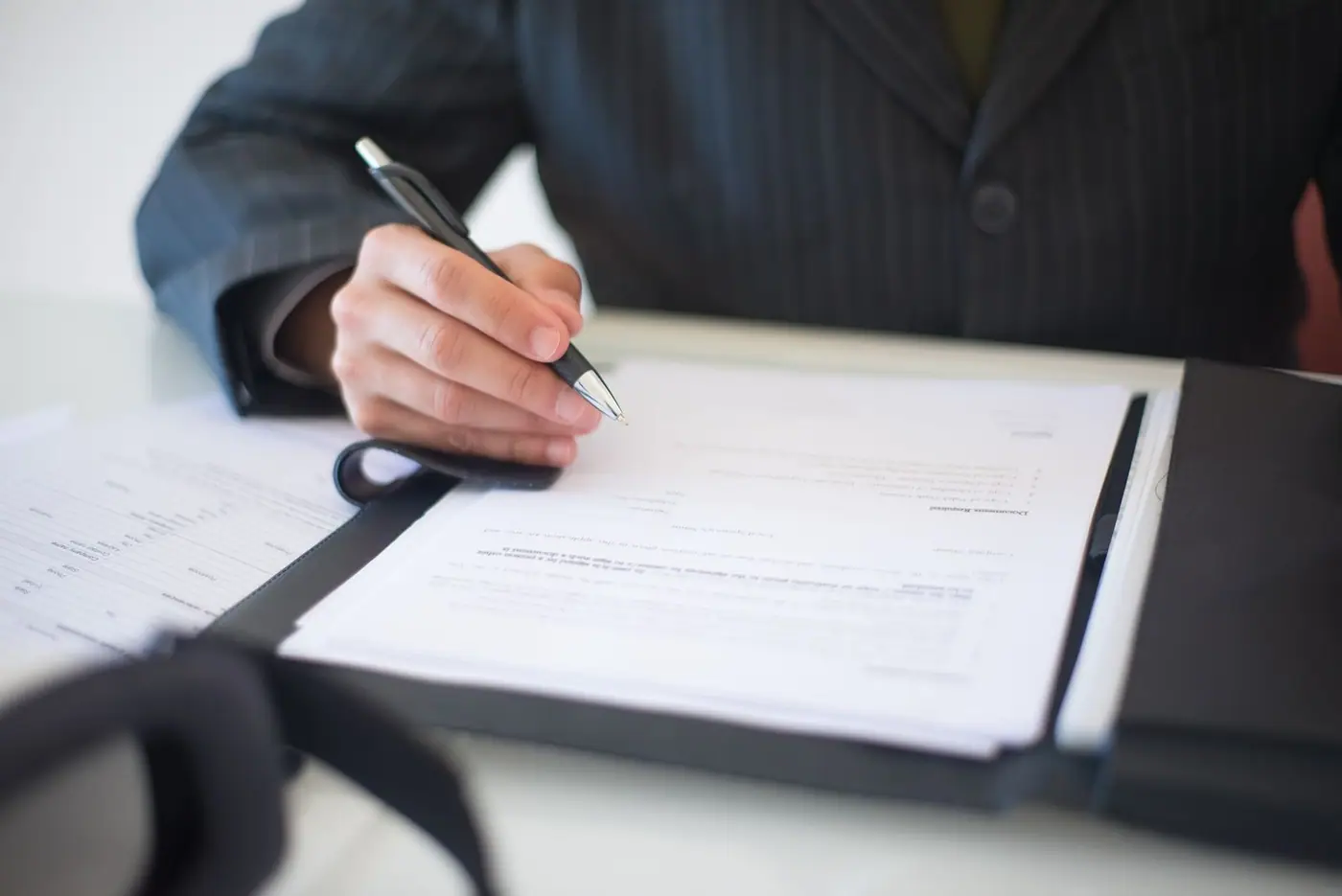 Close-up of a hand signing documents with a pen.