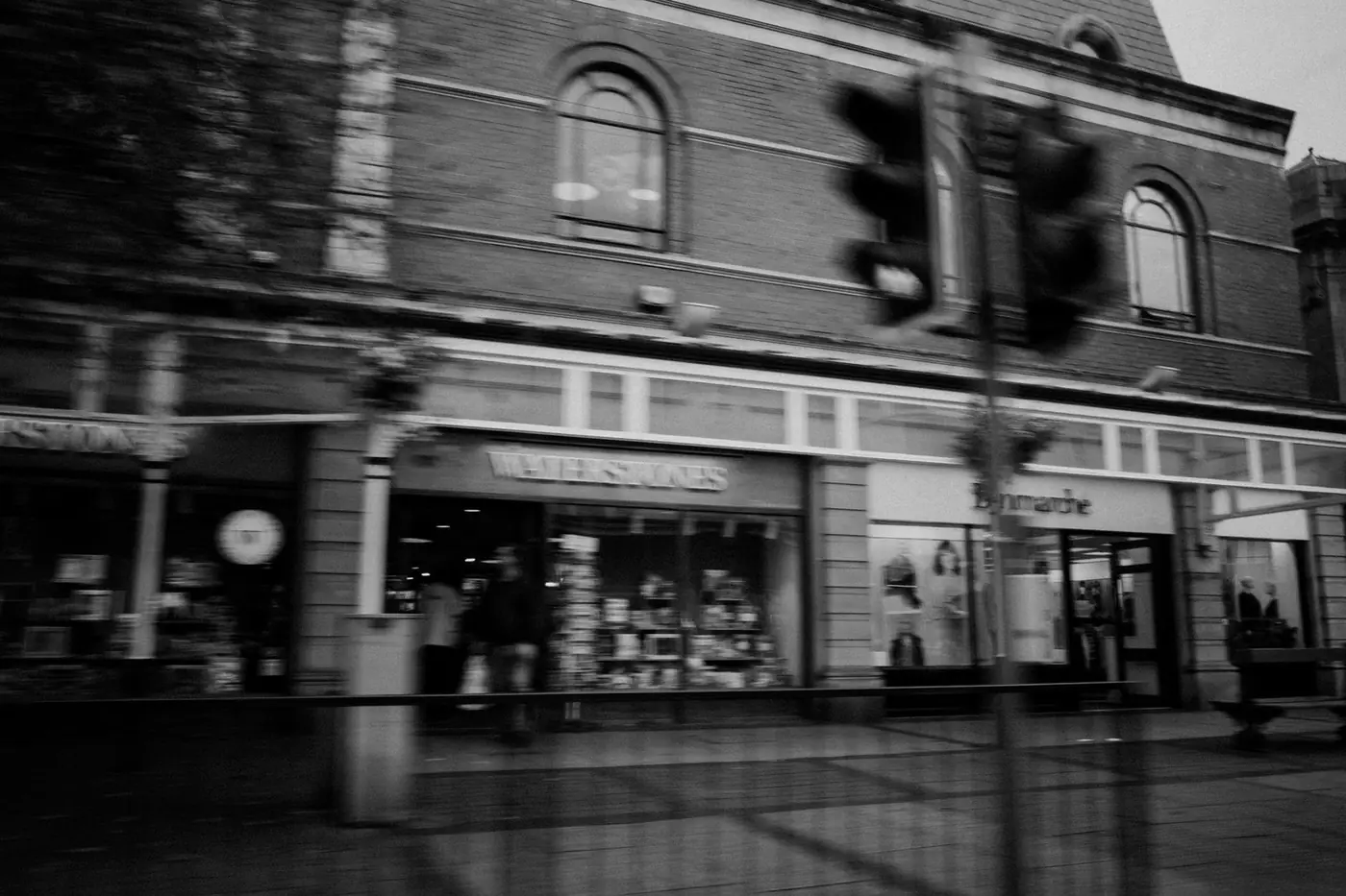 A busy high street in black and white, with shops and people blurred in motion