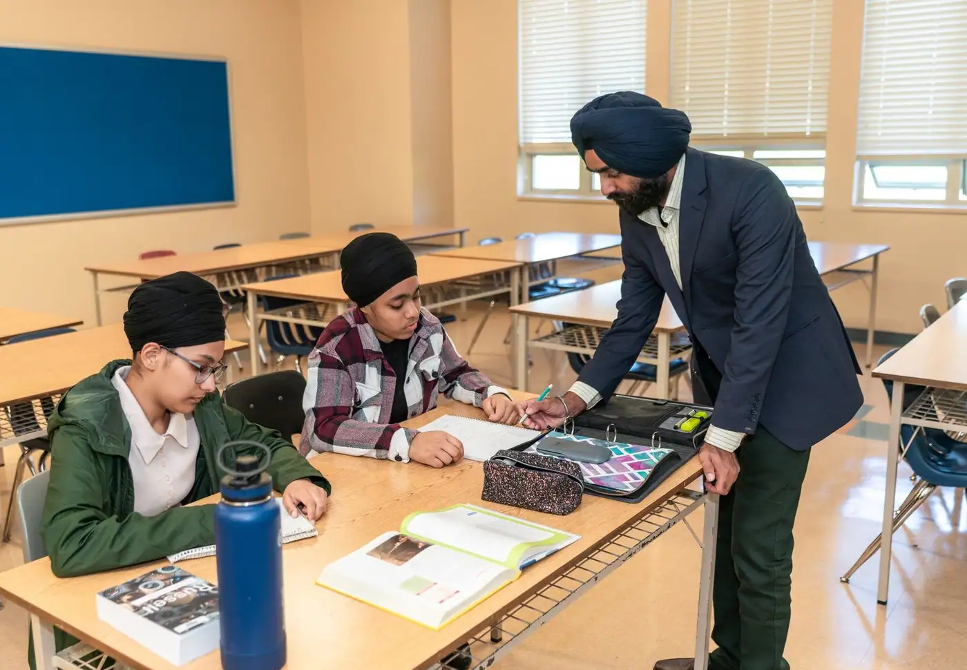 A teacher helps two students with homework in a bright classroom.