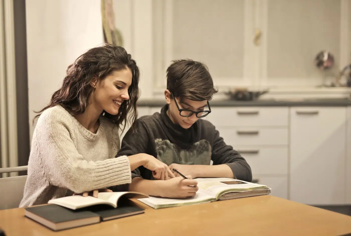A young woman helping a younger boy with homework at a table with books.