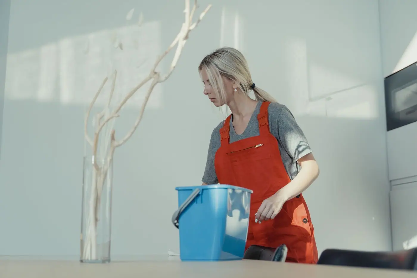 A cleaner in a red uniform cleaning indoors with a blue bucket