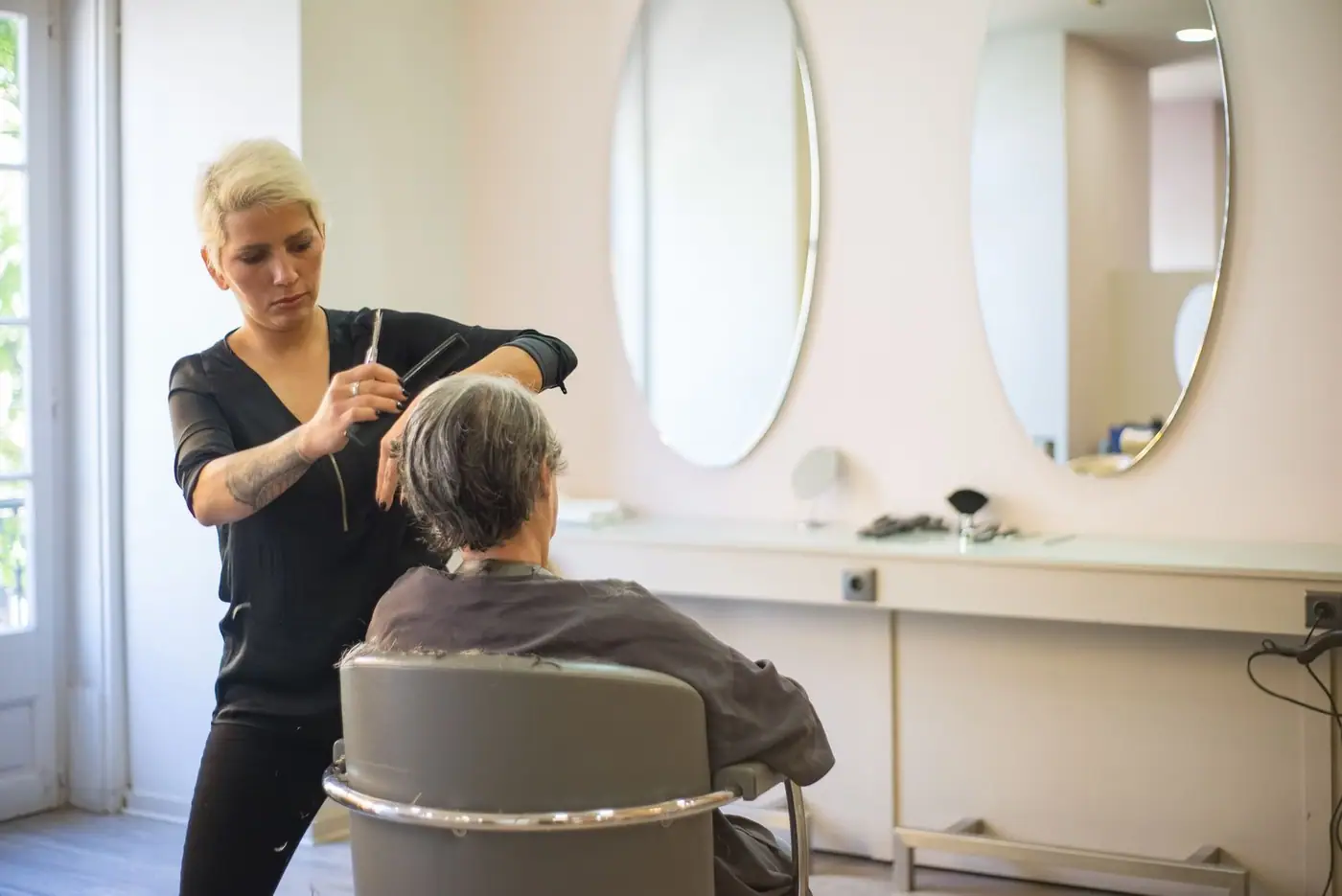 A hairdresser cuts a woman's hair in a modern salon with mirrors and a barber chair
