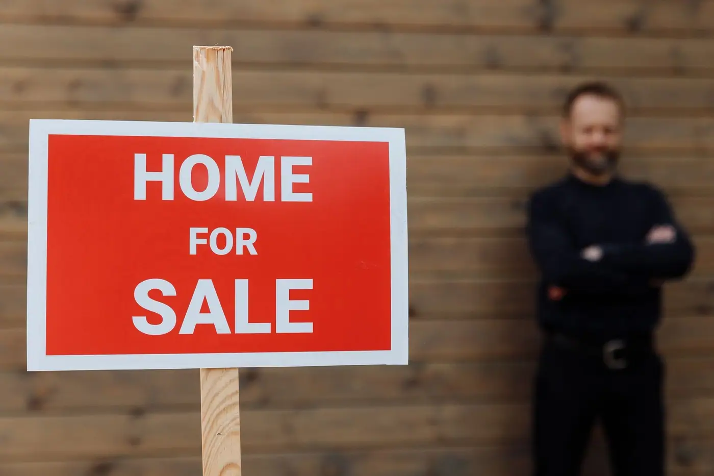 A home for sale sign beside a wooden wall.