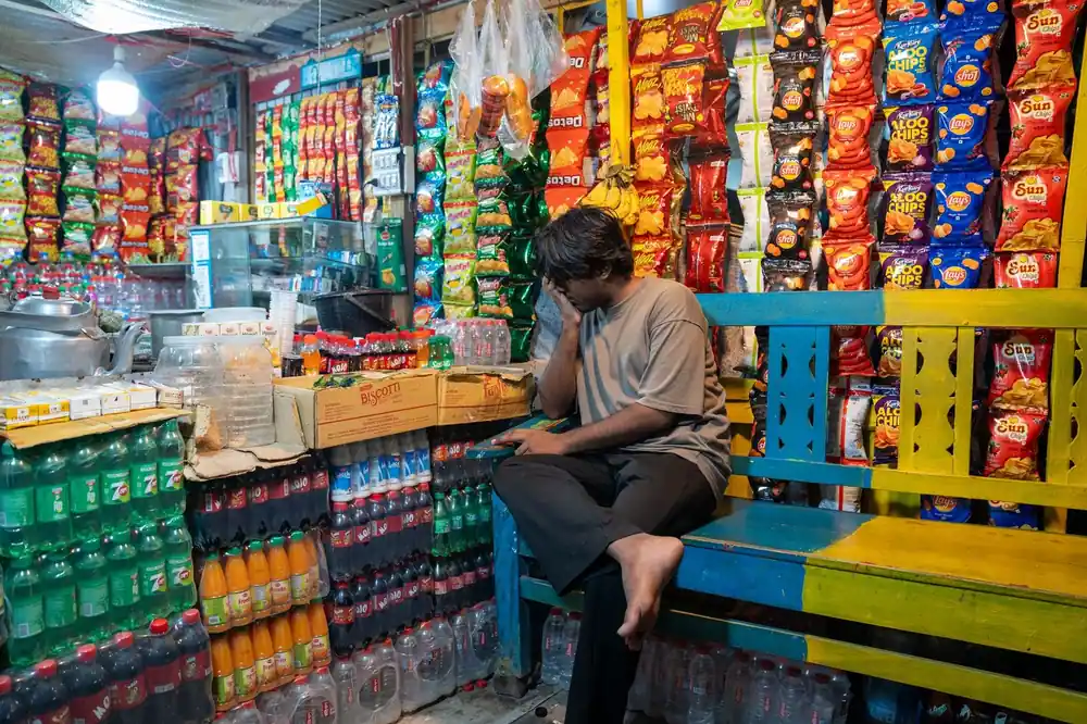 A vibrant Indian snack shop filled with colorful packaged goods and drinks. An adult man sits thoughtfully.