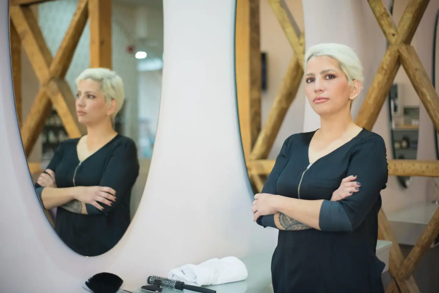 A hairdresser standing with arms crossed in a modern salon, reflected in a mirror