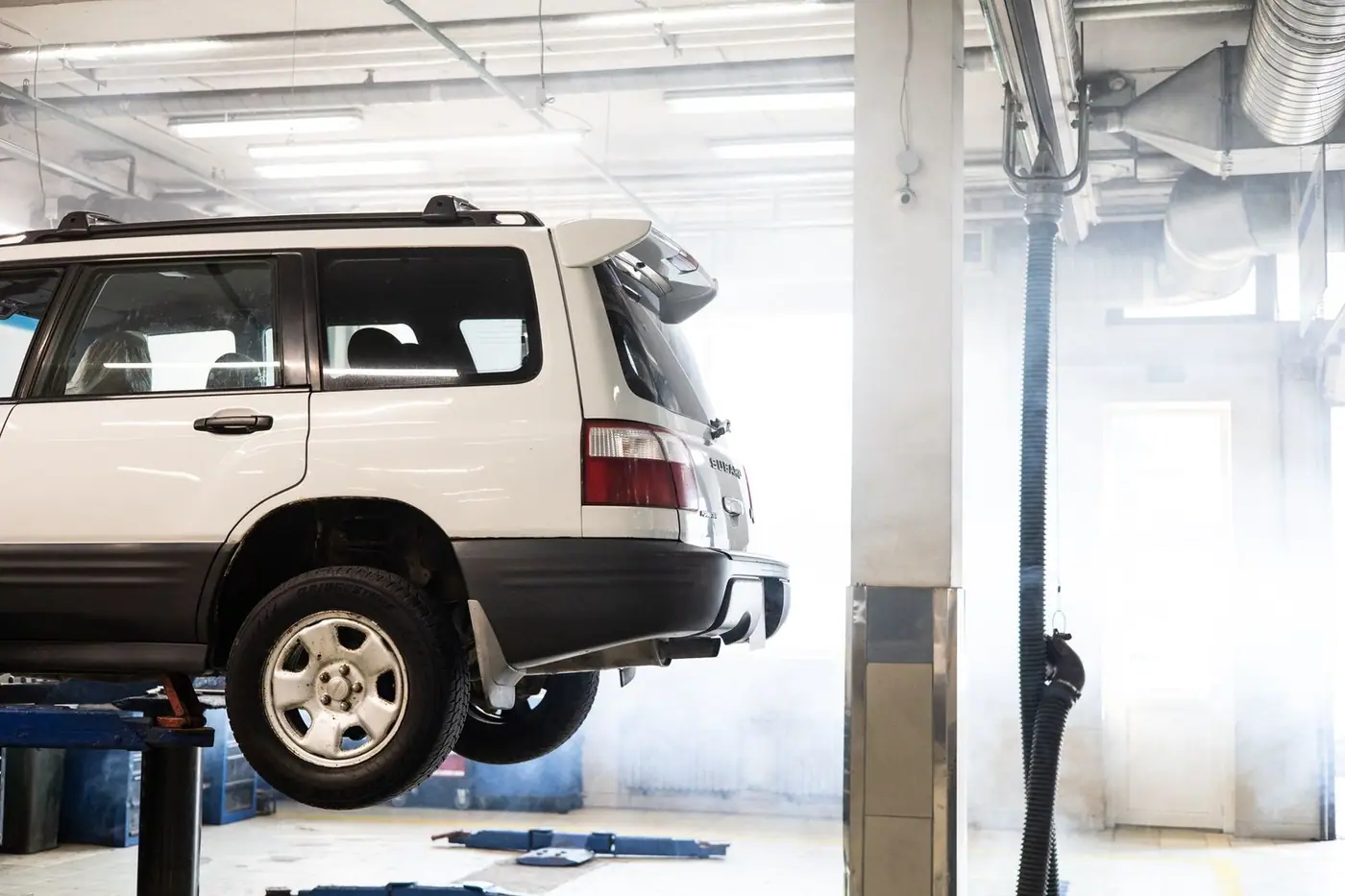 A white SUV raised on a lift inside a repair workshop