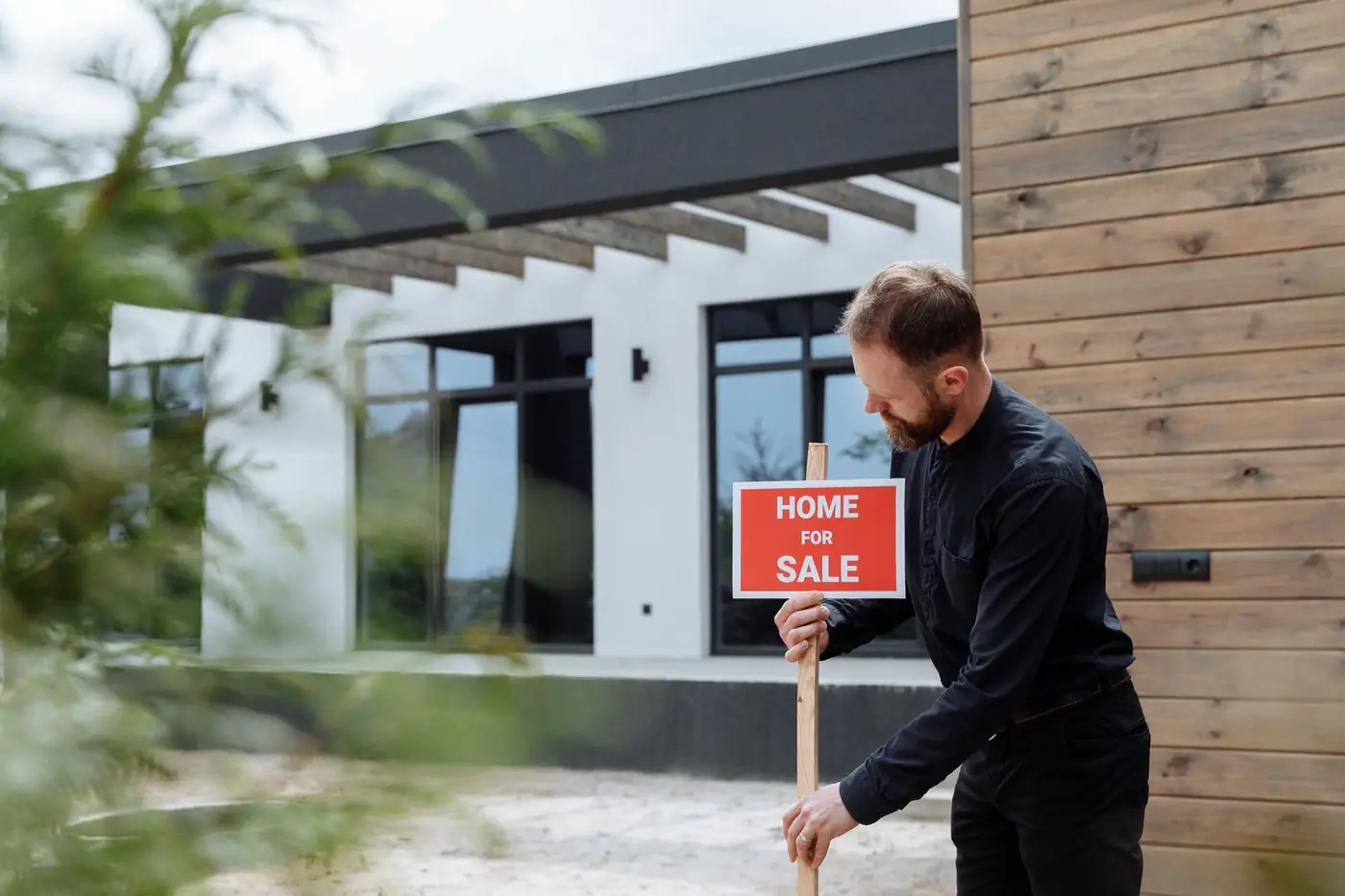 A man placing a home for sale sign outside a modern house.