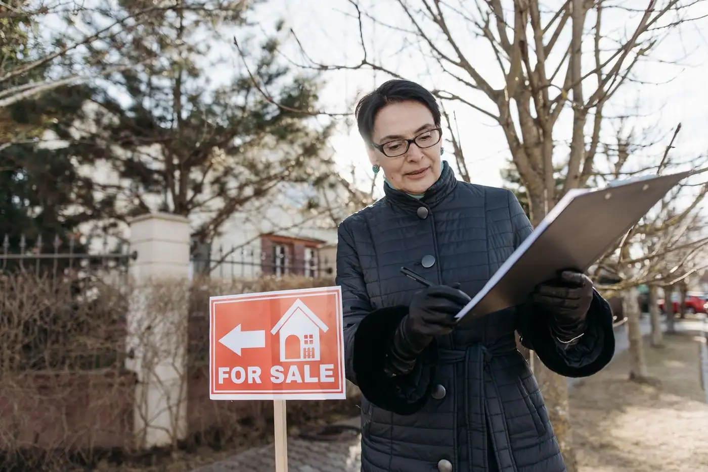 A clipboard being reviewed beside a For Sale sign outside a property on a clear day.