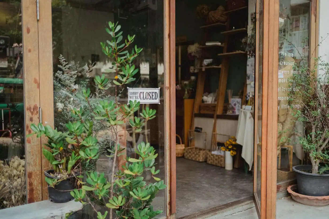 Exterior of a contemporary glass-walled store with an open door and potted plants in daylight