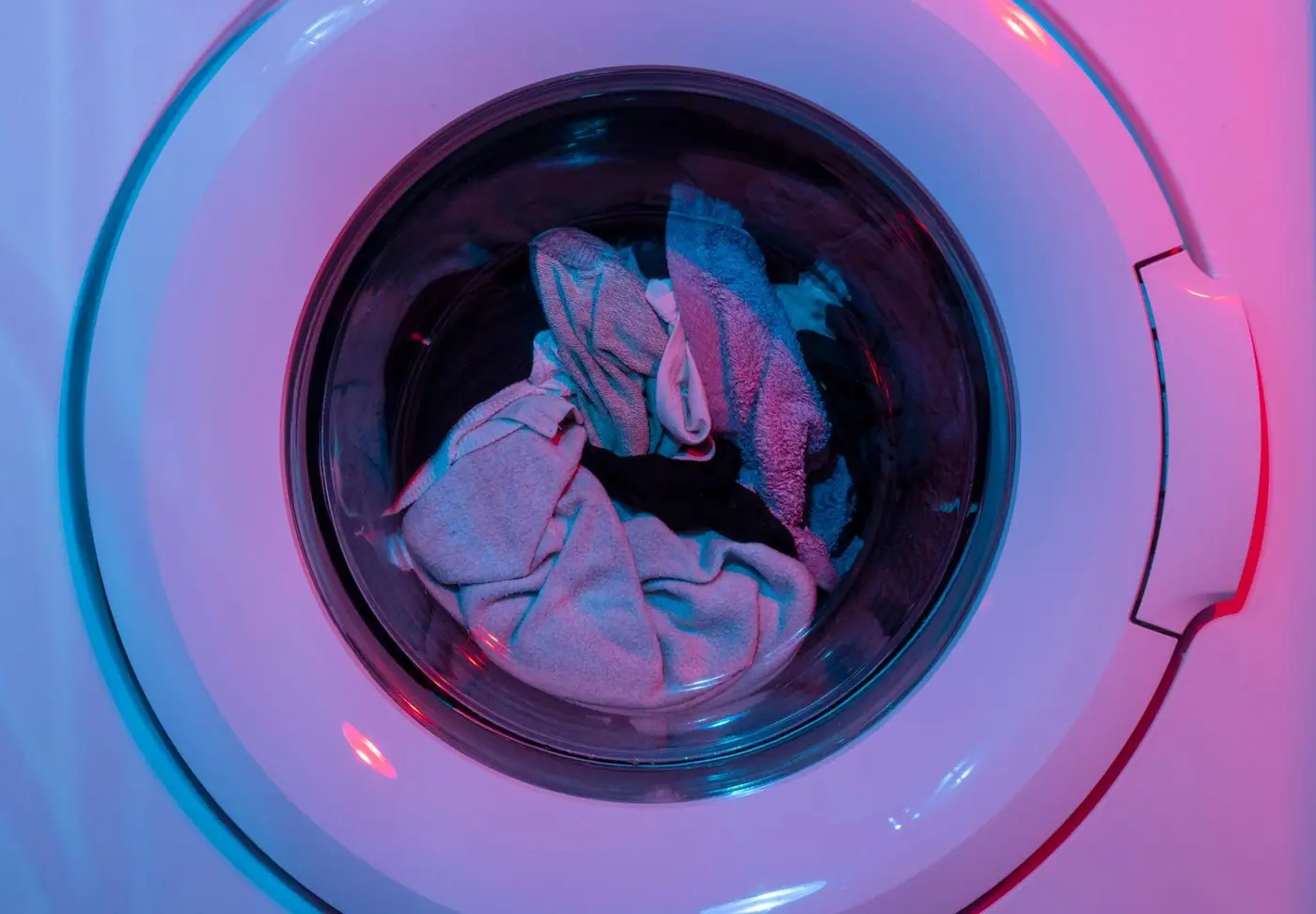 Colourful washing machine with clothes inside, lit by vivid purple and blue lights