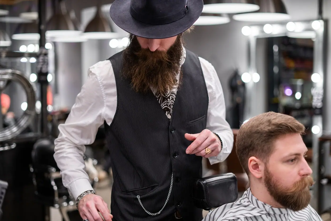 A bearded barber trimming a client's hair in a modern barbershop