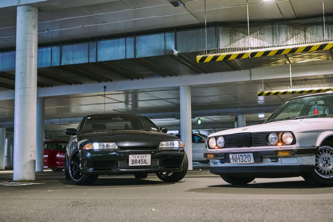 Two modified sports cars in a dimly lit multi-storey car park