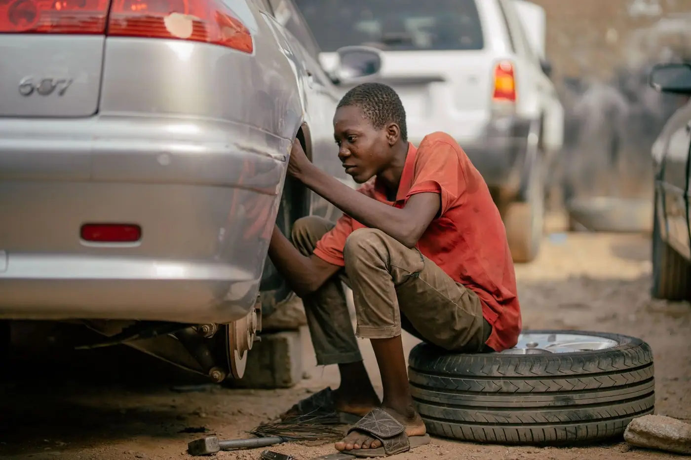 A young mechanic focused on repairing a car tyre in an outdoor garage