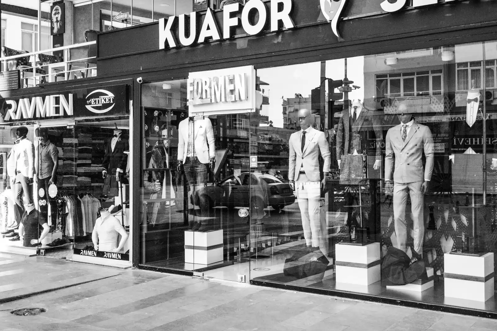 Black and white image of a men's fashion storefront showcasing elegant suits with mannequins prominently featured.