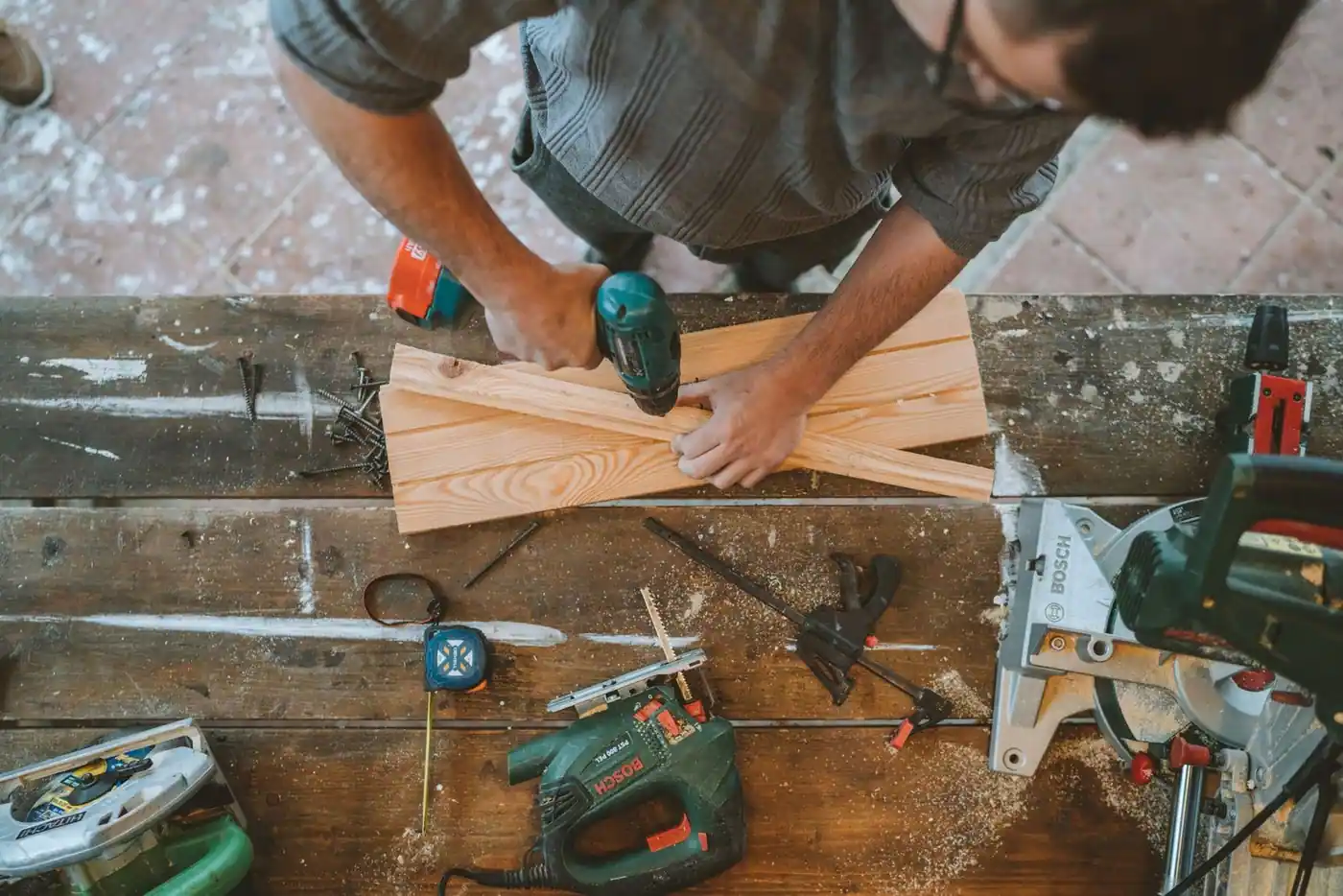 Craftsman drilling wooden planks in a carpentry workshop surrounded by tools