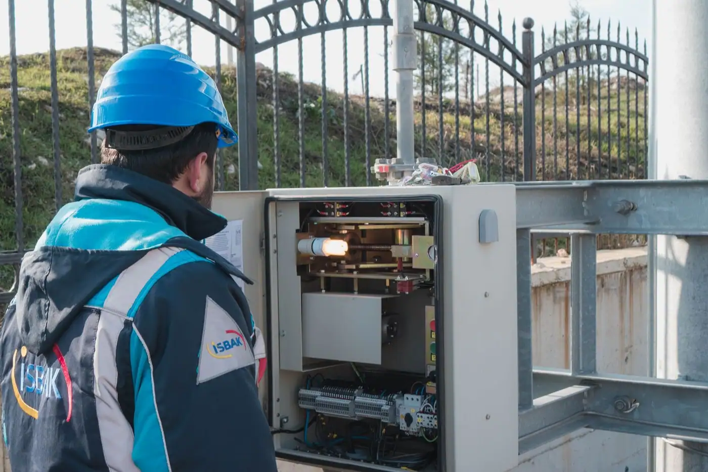 An electrician in a hard hat inspecting an outdoor fuse box.