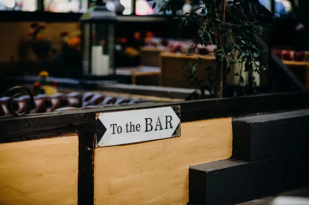 A close-up view of a 'To the BAR' sign in a warmly lit indoor lounge area.