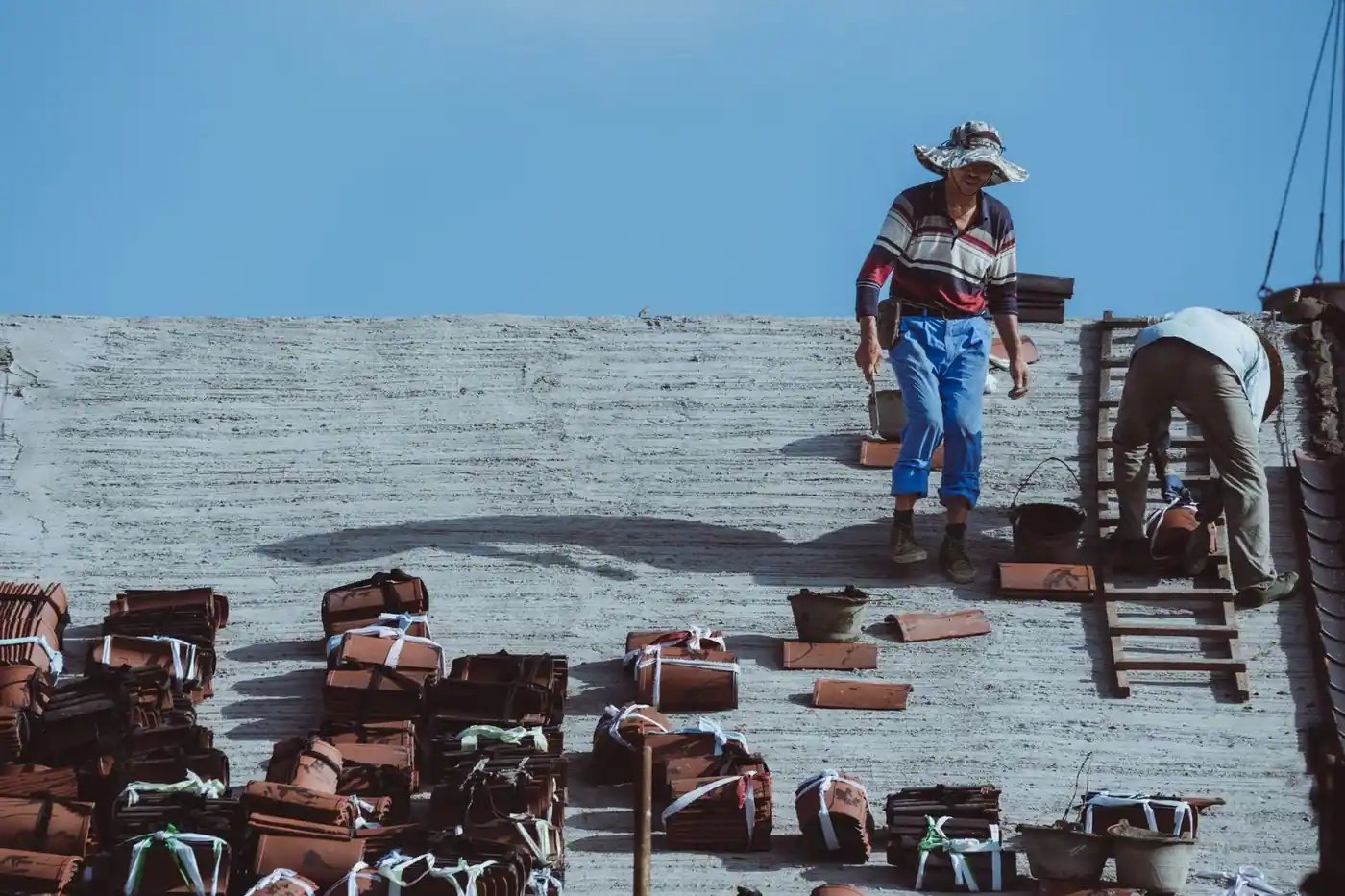 Two construction workers installing roof tiles under a clear blue sky