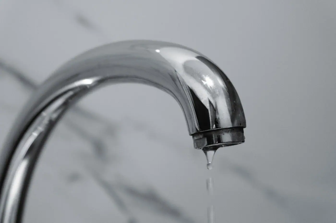 Close-up of a modern chrome bathroom tap with water dripping from the tip