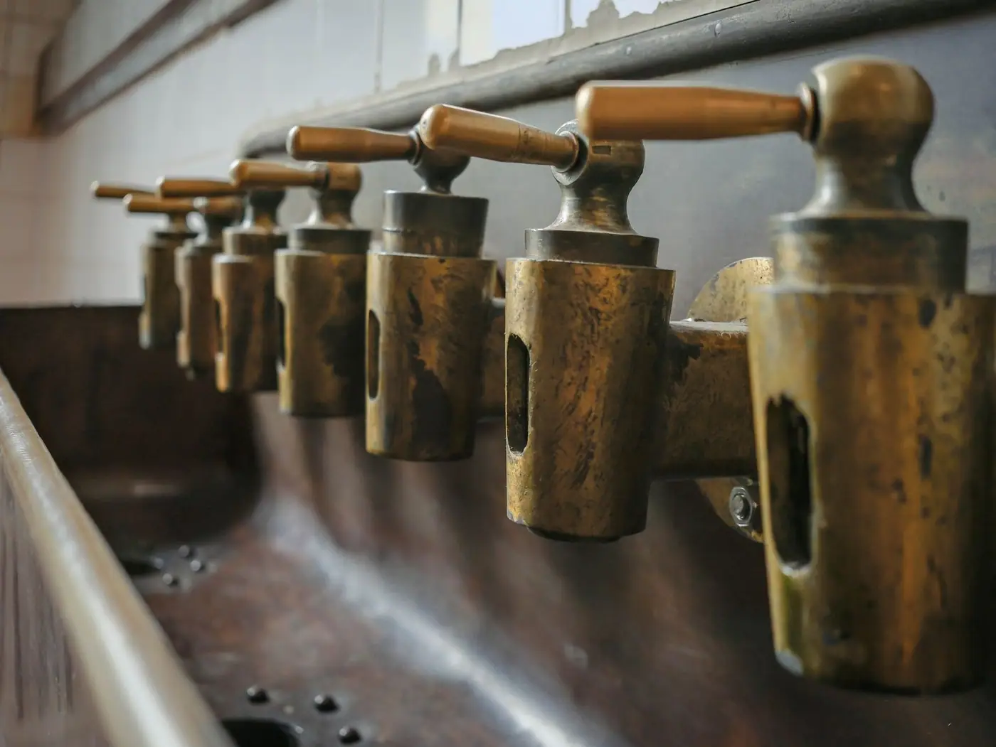 A row of aged brass taps with wooden handles in an industrial setting