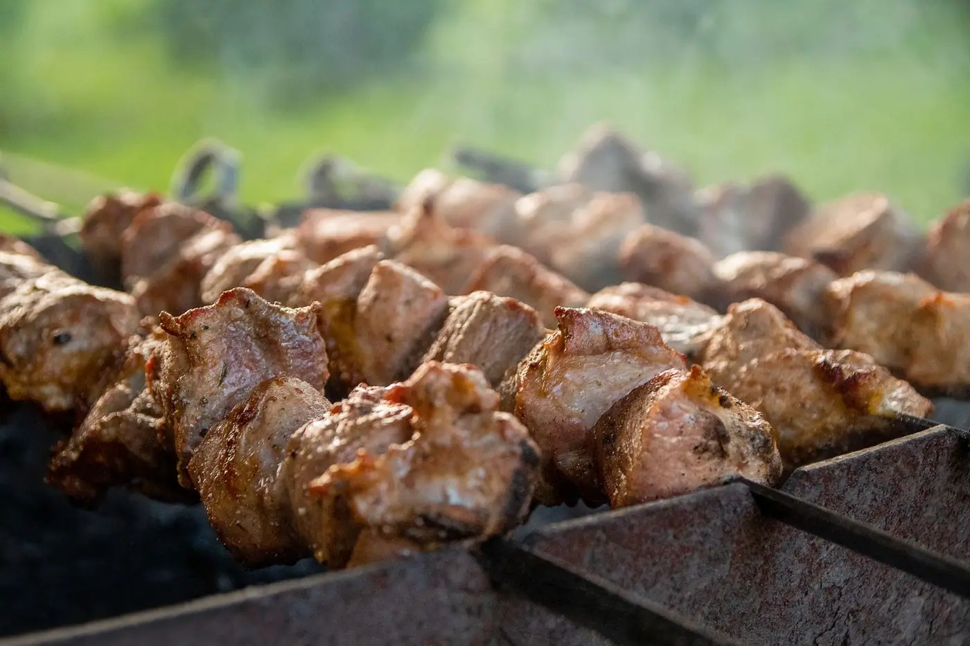Juicy skewers of meat sizzling on a hot charcoal grill with smoke rising