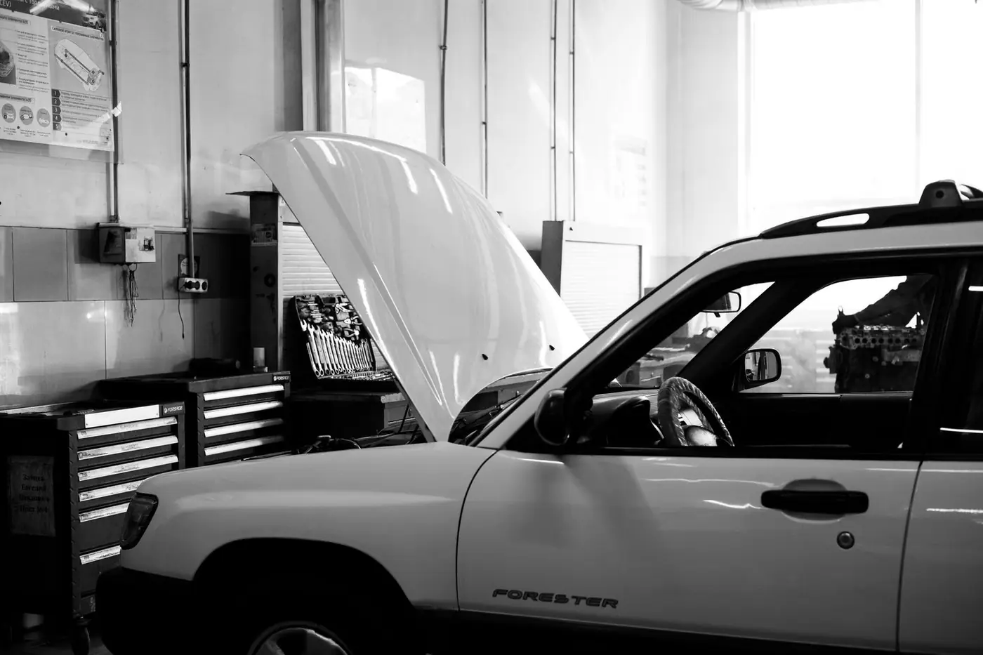 Black and white photo of a car in an auto repair shop with its bonnet open for maintenance
