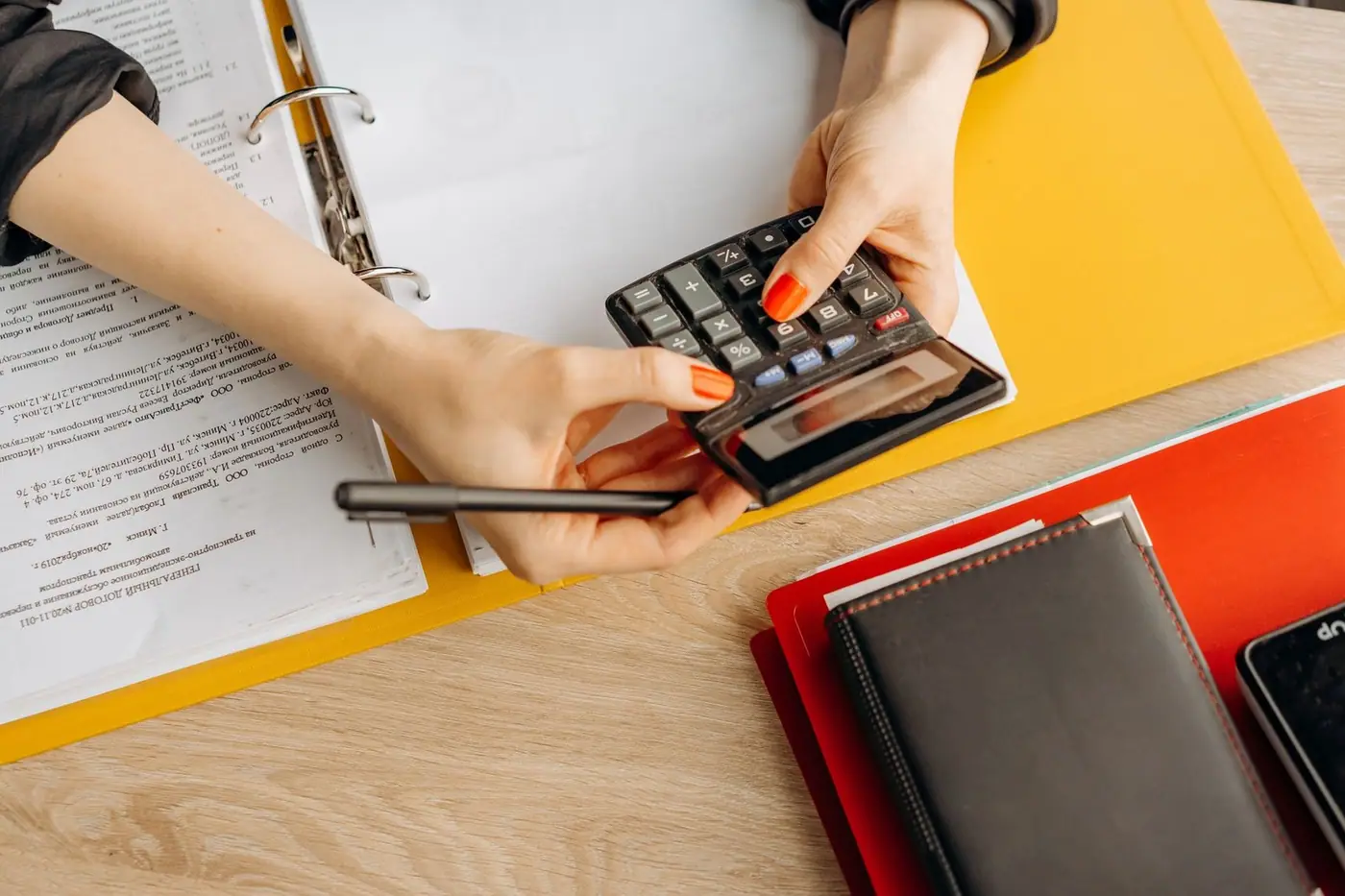 Hands using a calculator at a desk with documents and folders
