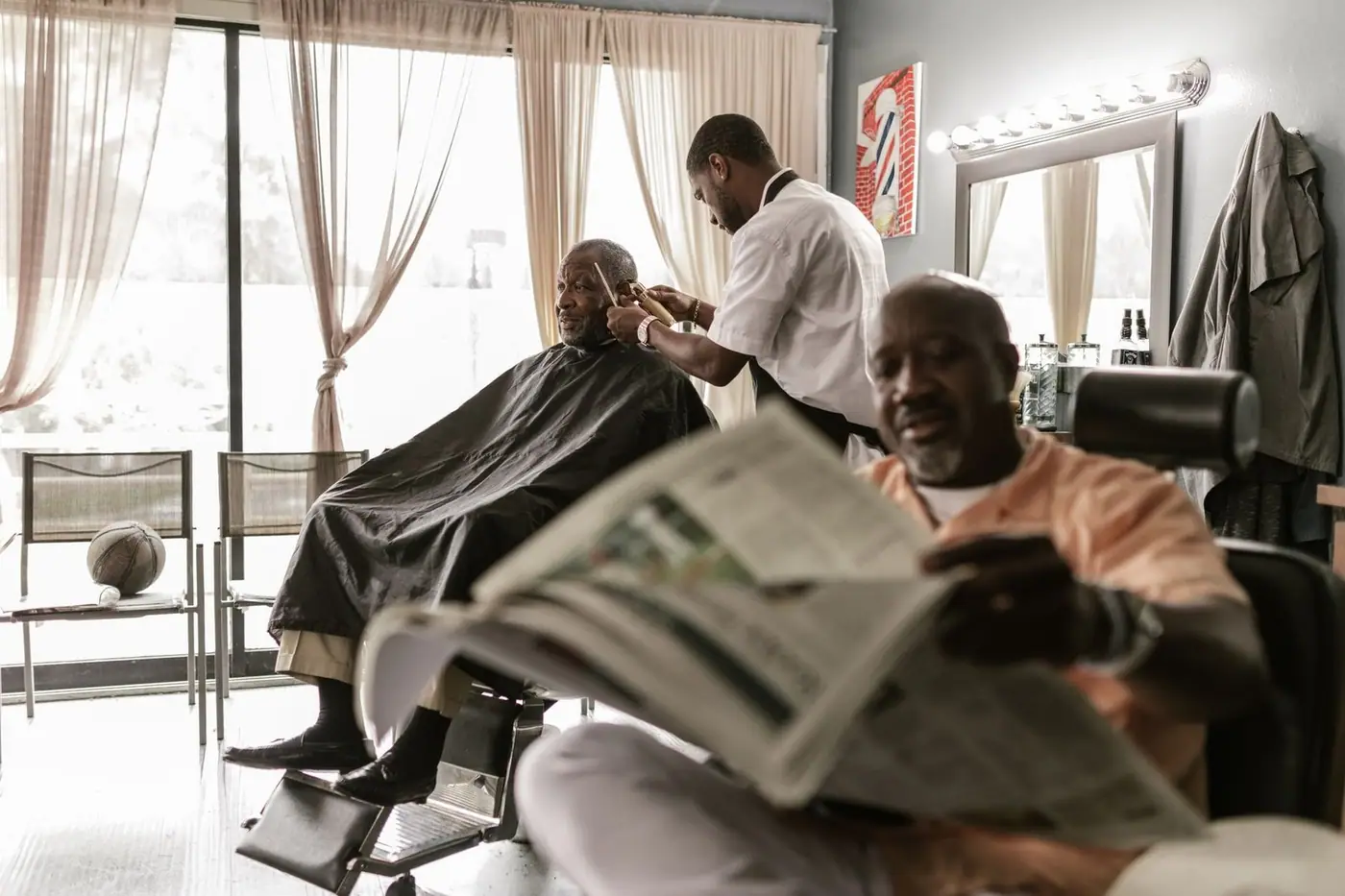 Two men relaxing at a barber shop while getting a haircut and reading newspapers