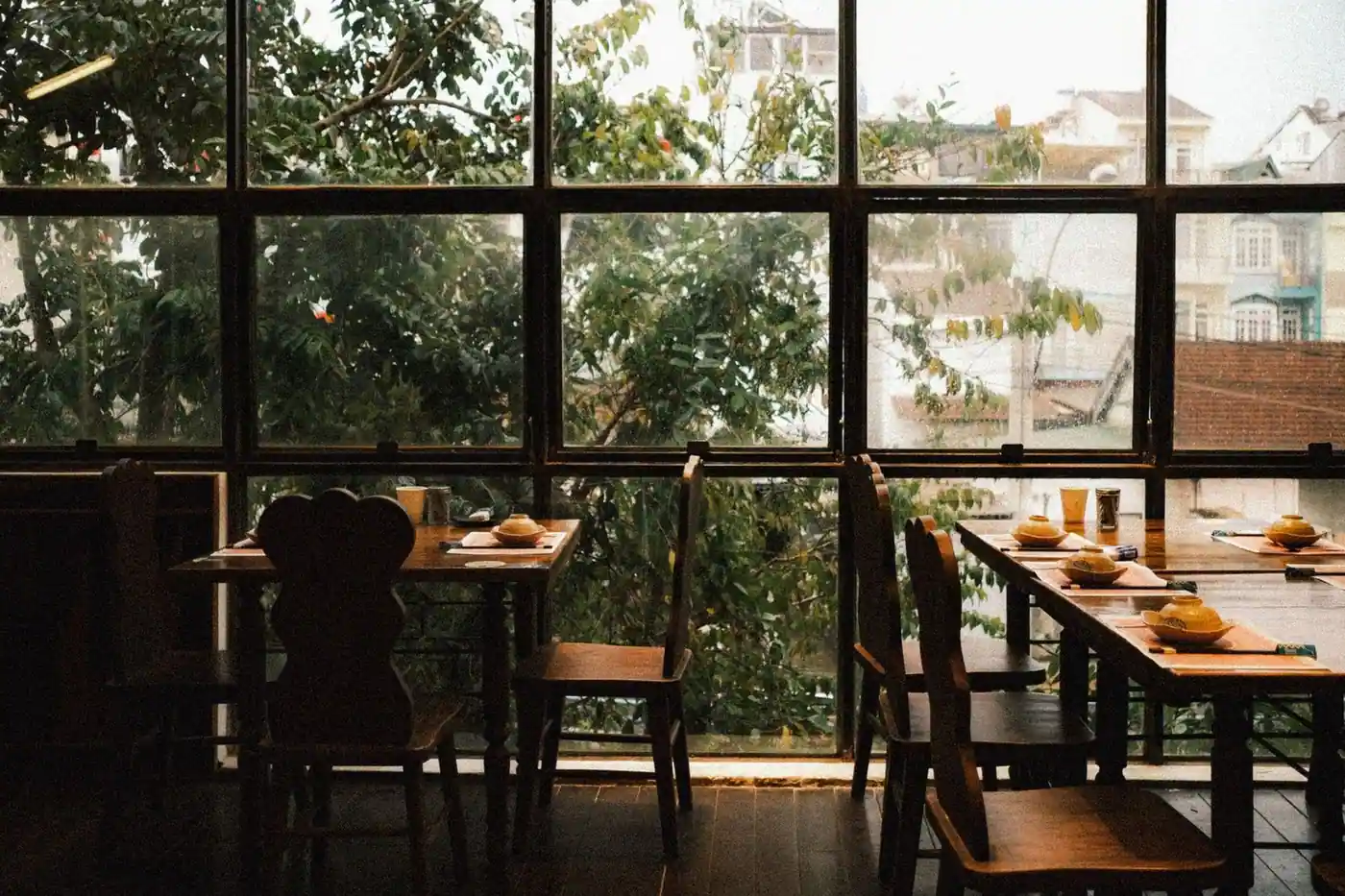 Warm and inviting restaurant interior with rustic wooden tables and chairs and a view of greenery through large windows