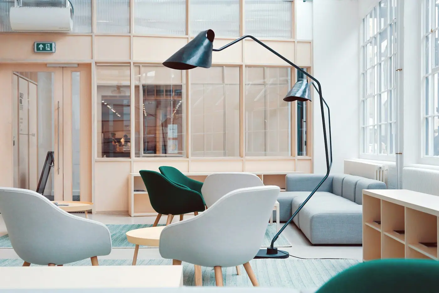 Light grey and green armchairs and a modern sofa around round wooden tables, with a tall angular black floor lamp