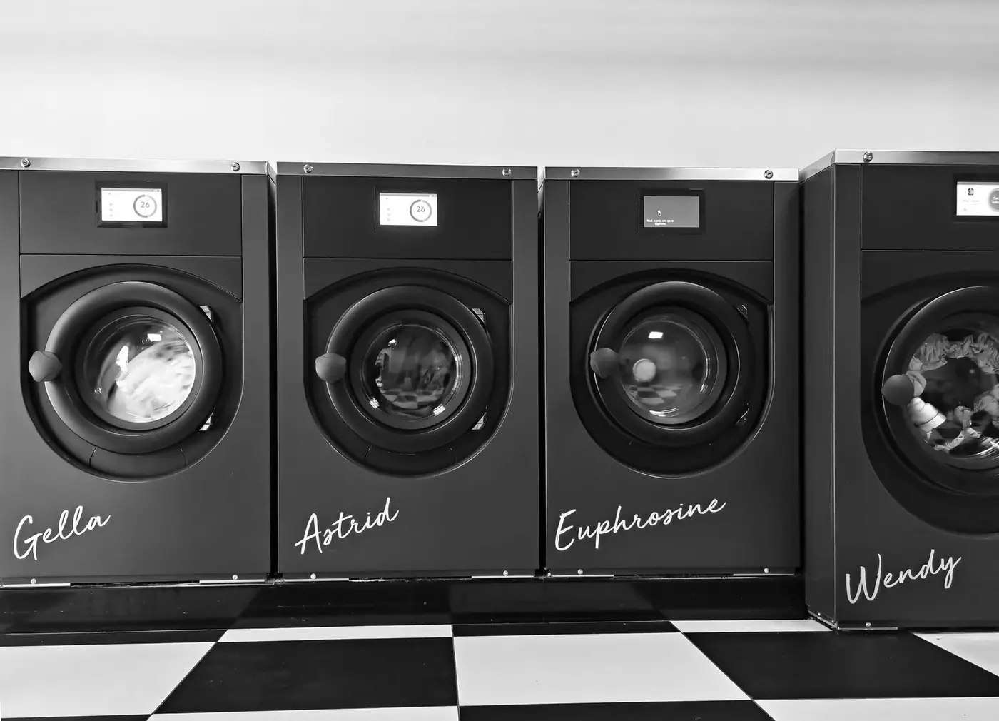 Grayscale image of four modern washing machines in a self-service laundry