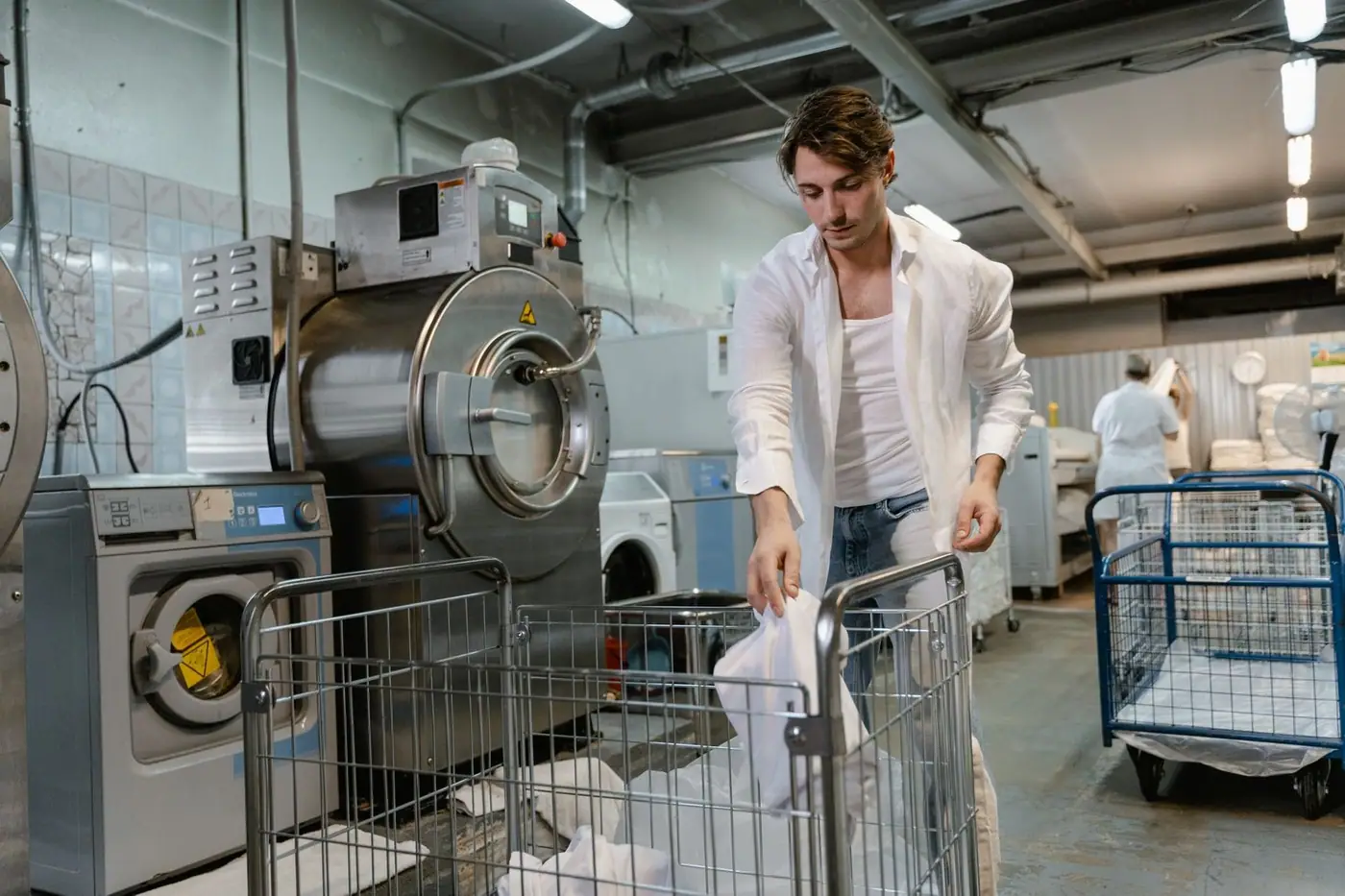 A man organising laundry in an industrial facility with machines and carts