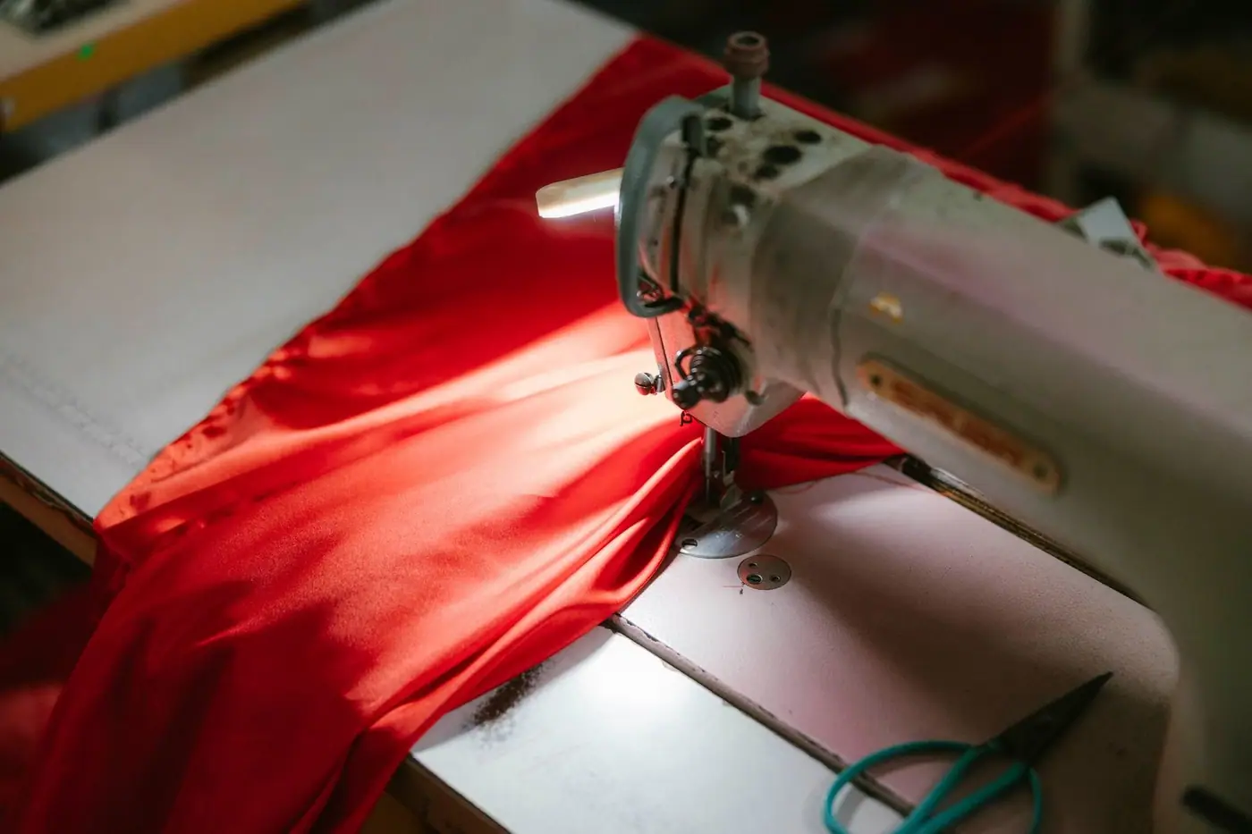 An industrial sewing machine stitching bright red fabric under a spotlight