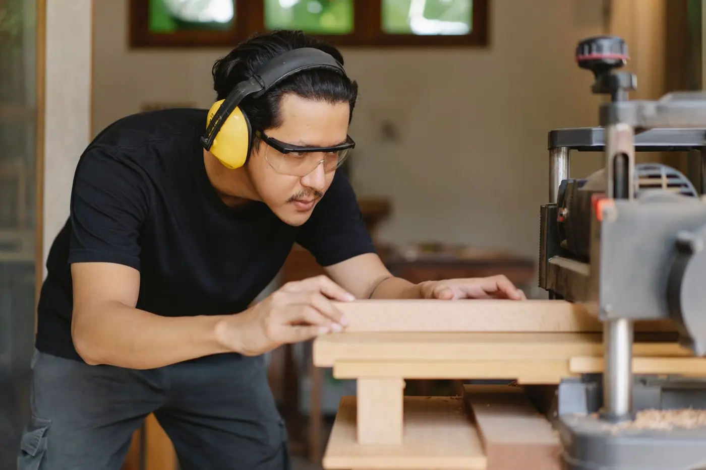 A tradesman in ear defenders and safety glasses flattening timber on a machine
