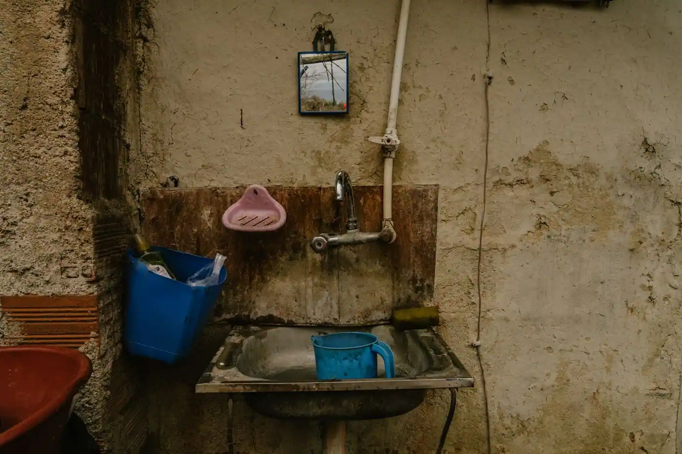 A rustic outdoor sink with vintage fittings and a small mirror reflecting the landscape