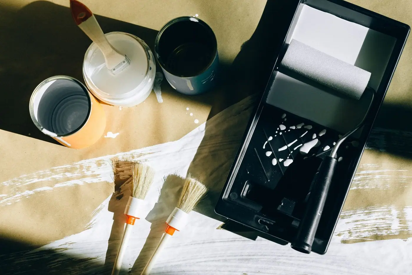 Top view of painting tools: brushes, rollers and paint cans laid out on paper.
