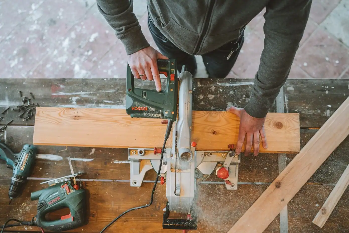 An electric jigsaw cutting a wooden plank, surrounded by tools