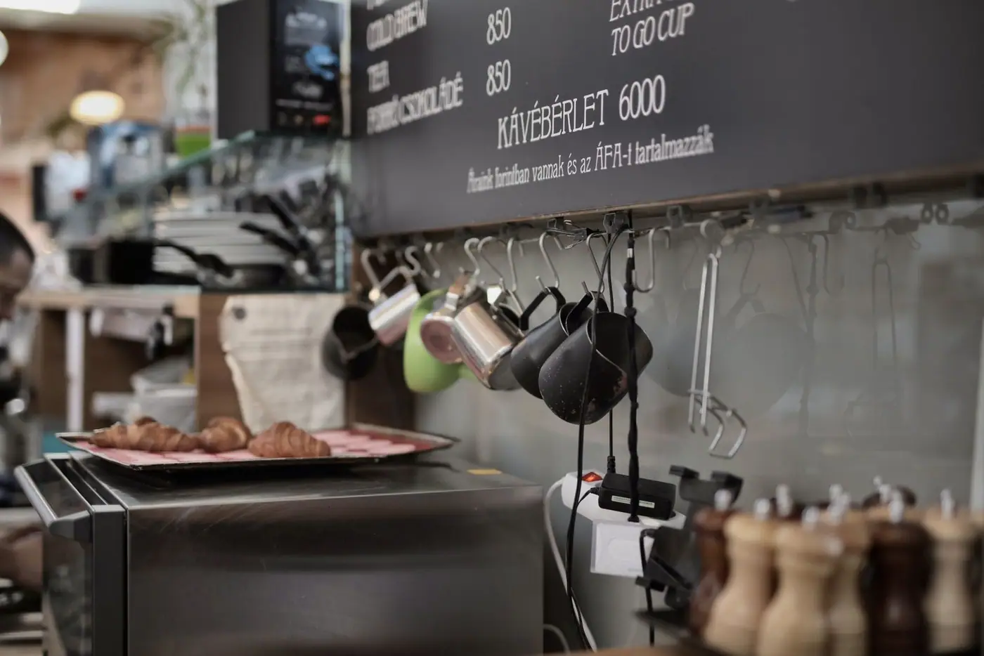 Metal cups hanging on hooks above an oven with a tray of freshly baked croissants