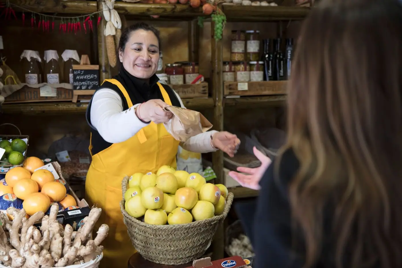 A smiling vendor handing a bag to a customer in a grocery shop