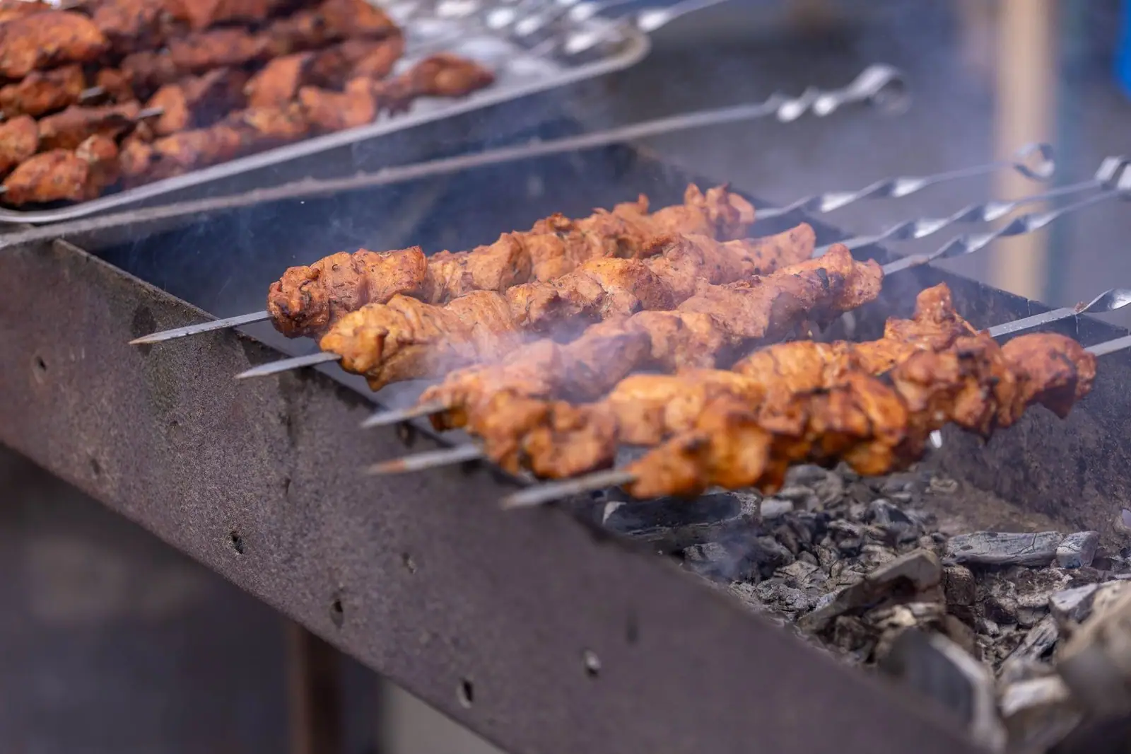 Close-up of skewered kebabs grilling over charcoal in an outdoor setting with smoke rising.